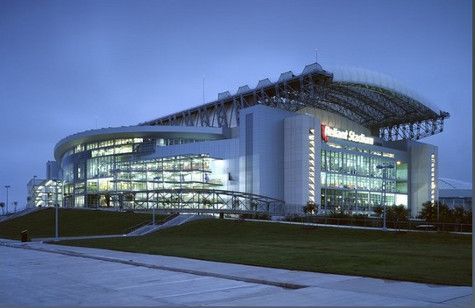 Modern stadium exterior with glass facade, illuminated at dusk; 