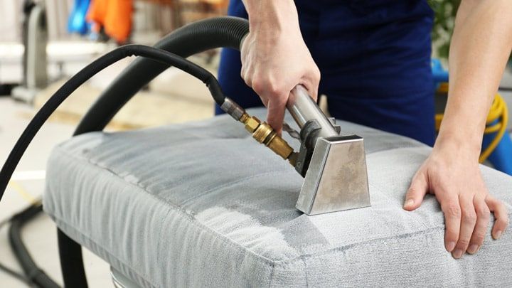 A couch is being cleaned using a vaccumm cleaner.