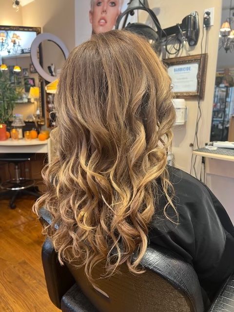 A woman with long curly hair is sitting in a chair in a salon.