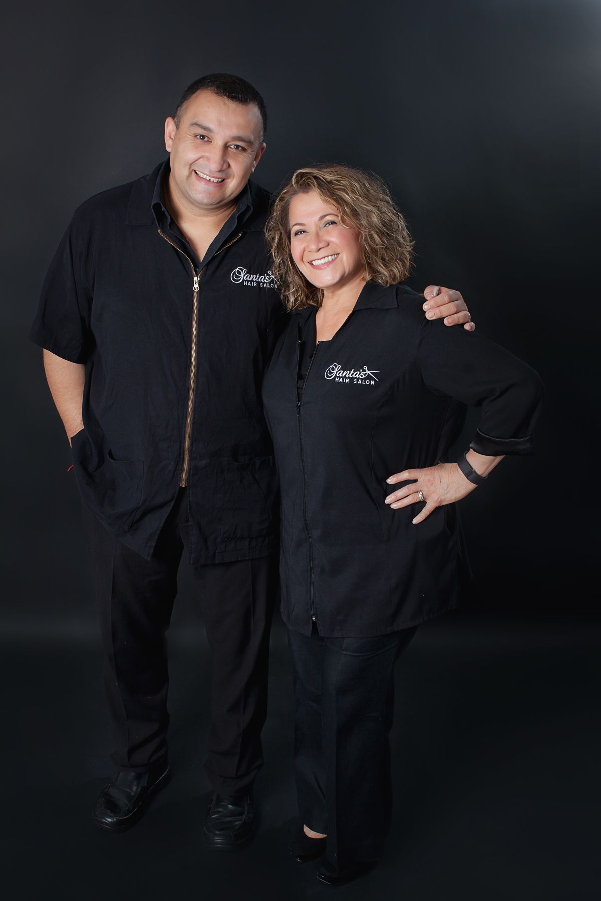 A man and a woman are posing for a picture in front of a black background.