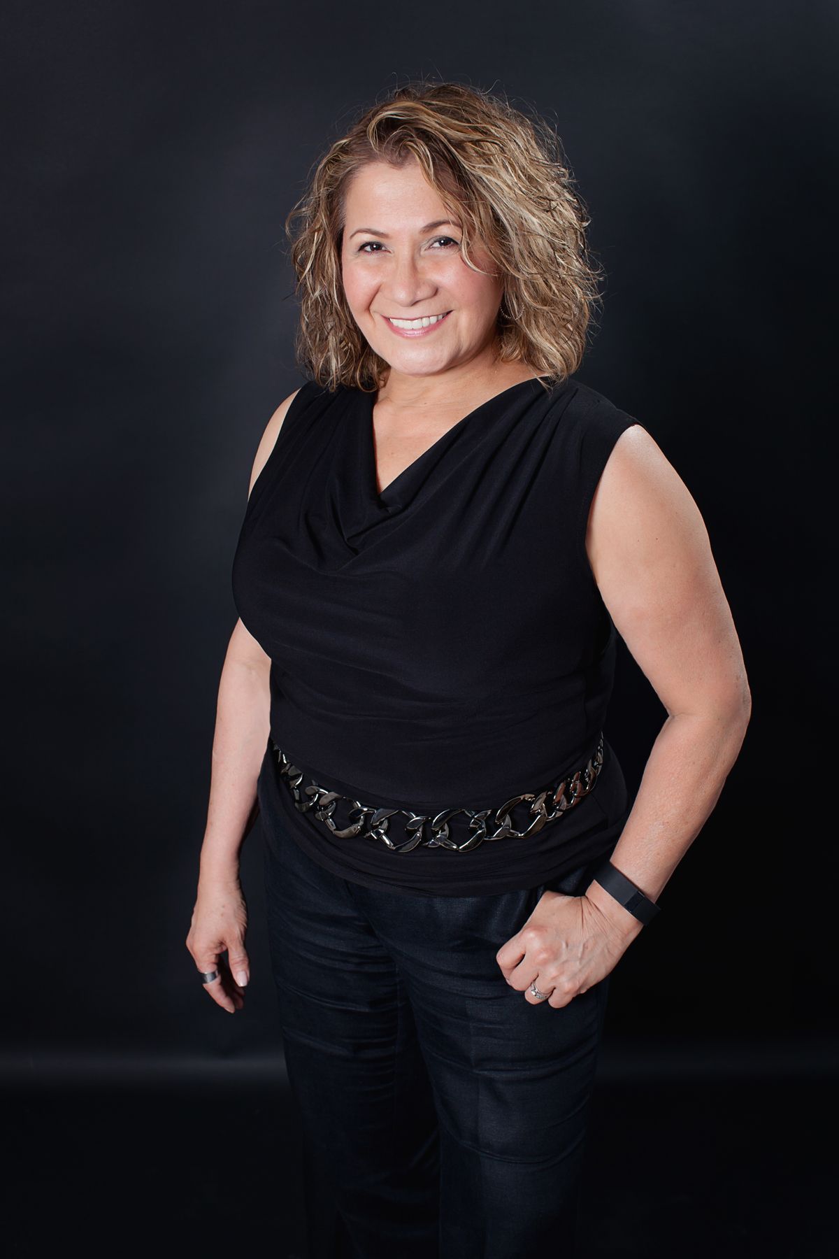 A woman in a black top and jeans is standing in front of a black background.