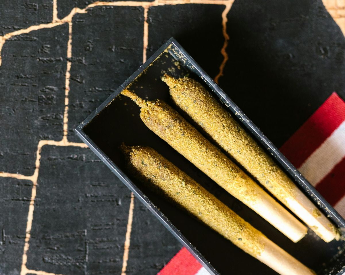 Two gold-dusted, cannabis-filled pre-rolled joints resting in a black rectangular box against a US map background.