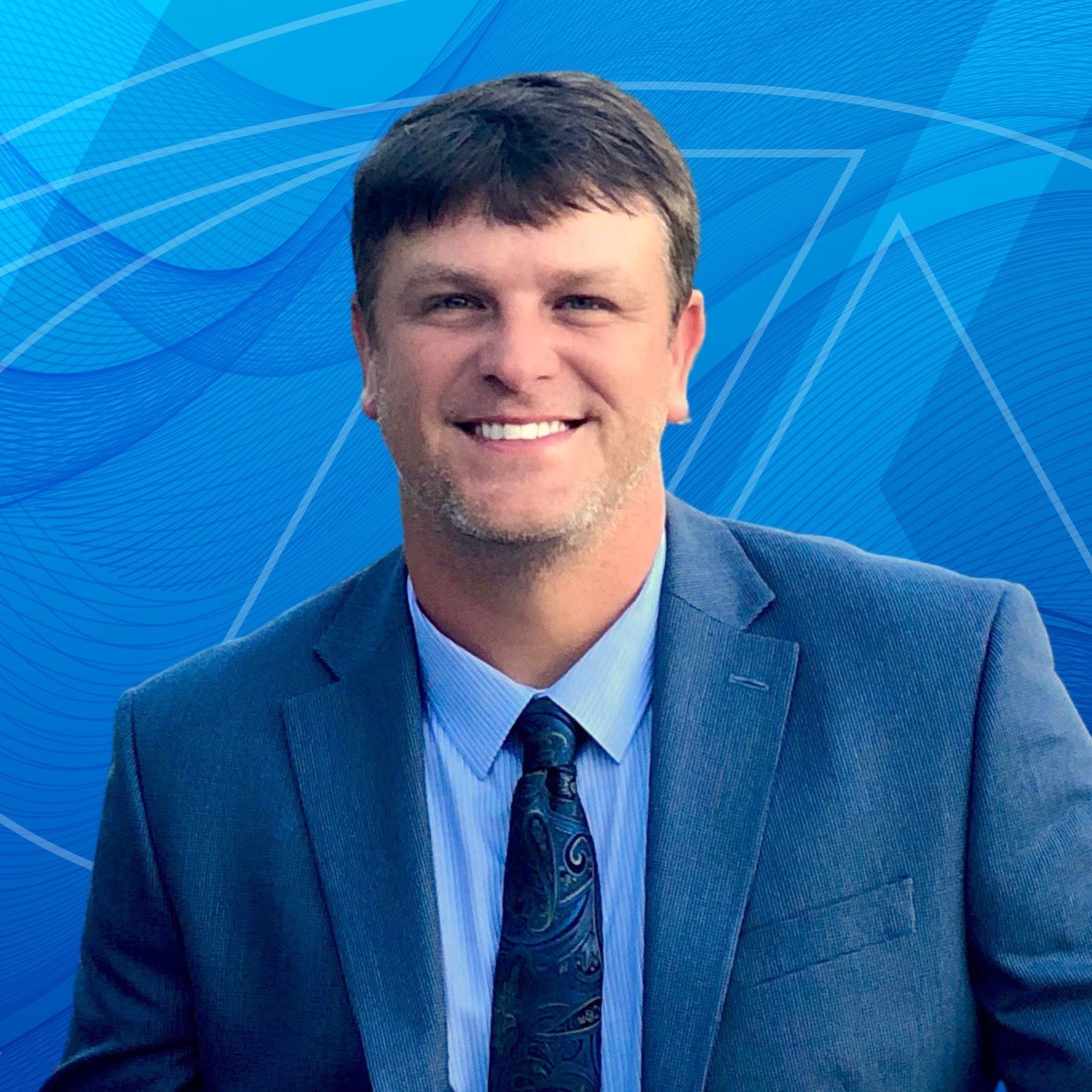 A man in a suit and tie is smiling in front of a blue background.