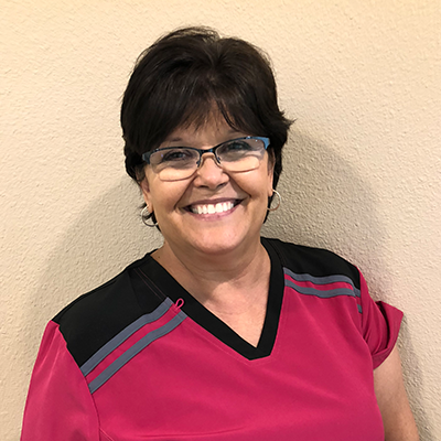 Woman in pink scrubs, glasses, and a smiling expression.