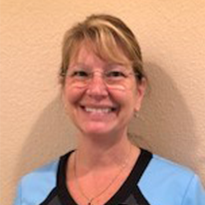 Woman with glasses smiles; blue top with black trim.