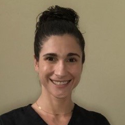 Woman with dark hair in a bun smiling, wearing a black shirt, against a beige wall.