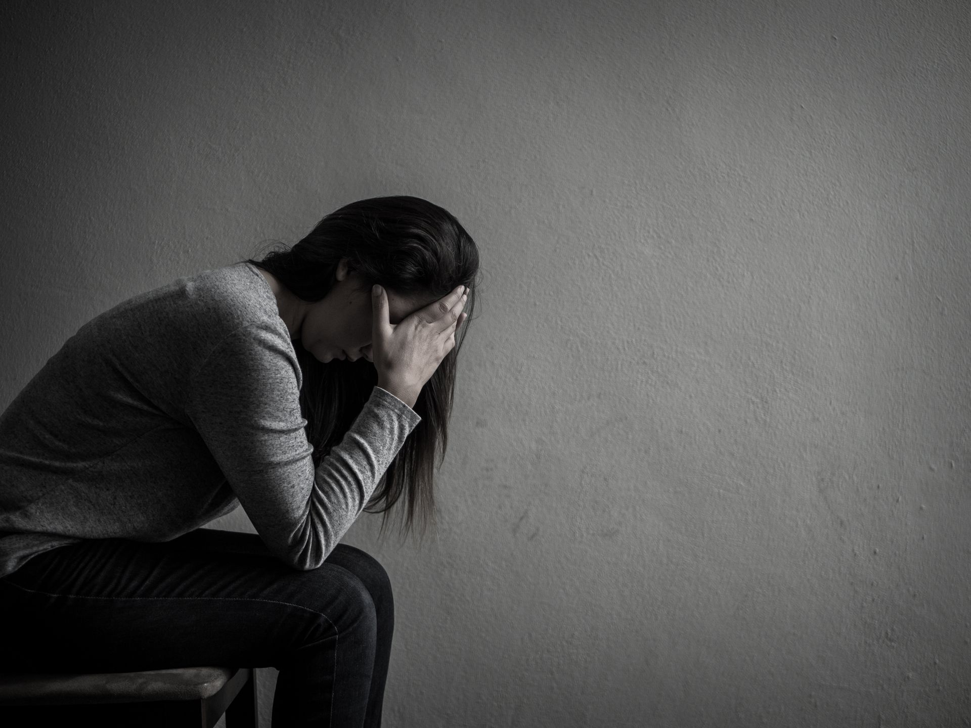 Person sitting and crying with head in hands against a plain wall