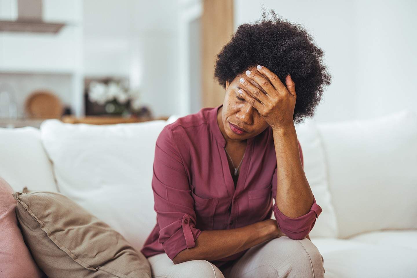 Woman on a white couch with her hand on her forehead, looking down with a sad expression.