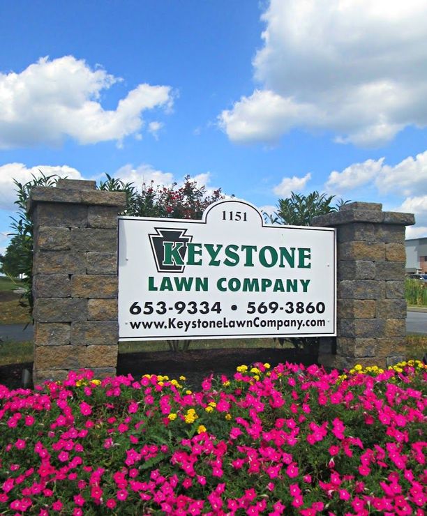 A sign for keystone lawn company is surrounded by pink flowers