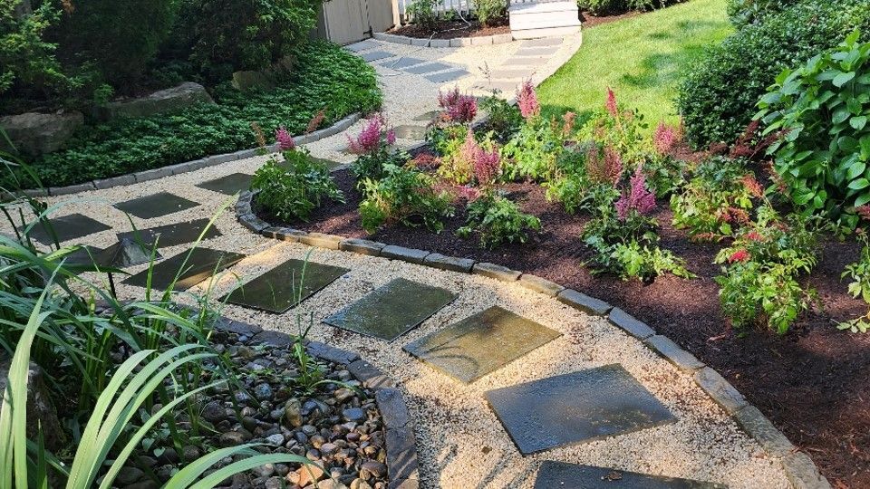 A stone walkway in a garden surrounded by flowers and plants.