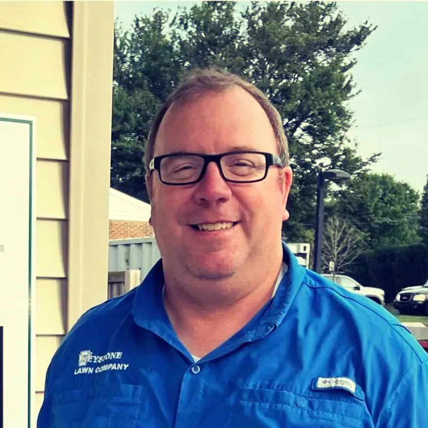A man wearing glasses and a blue shirt is smiling