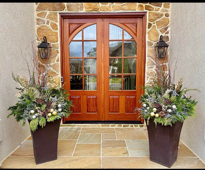 Pair of winter planters framing wooden double doors, stone facade, and lanterns.