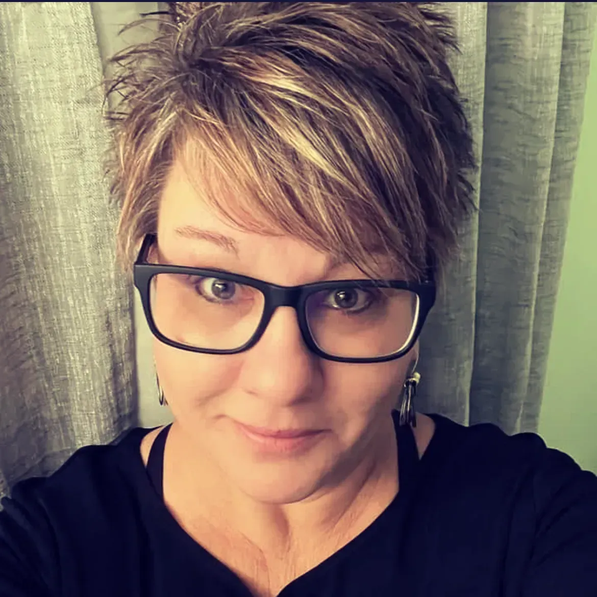 A woman wearing glasses and earrings is taking a selfie