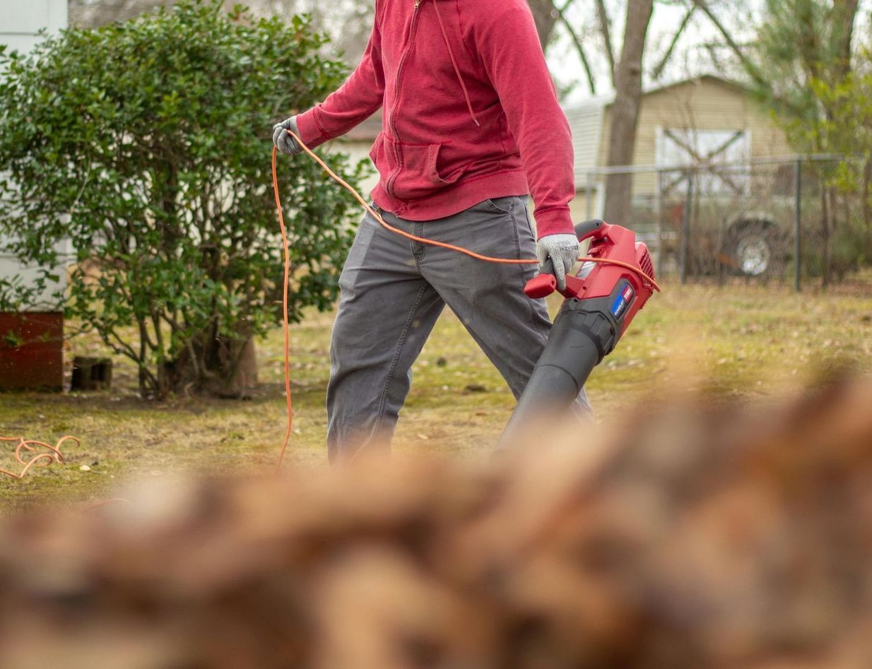 A man is standing in a yard holding a lawn mower.