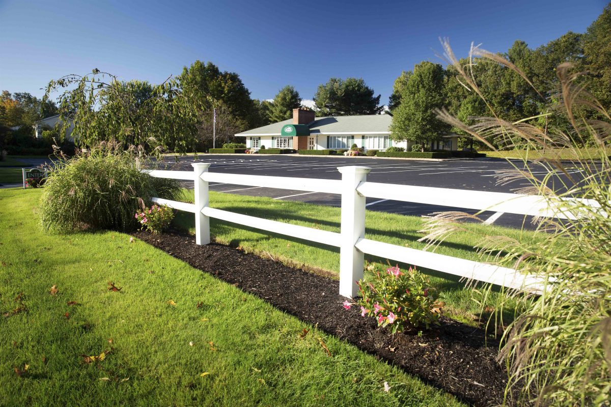 A white fence surrounds a lush green lawn in front of a house.