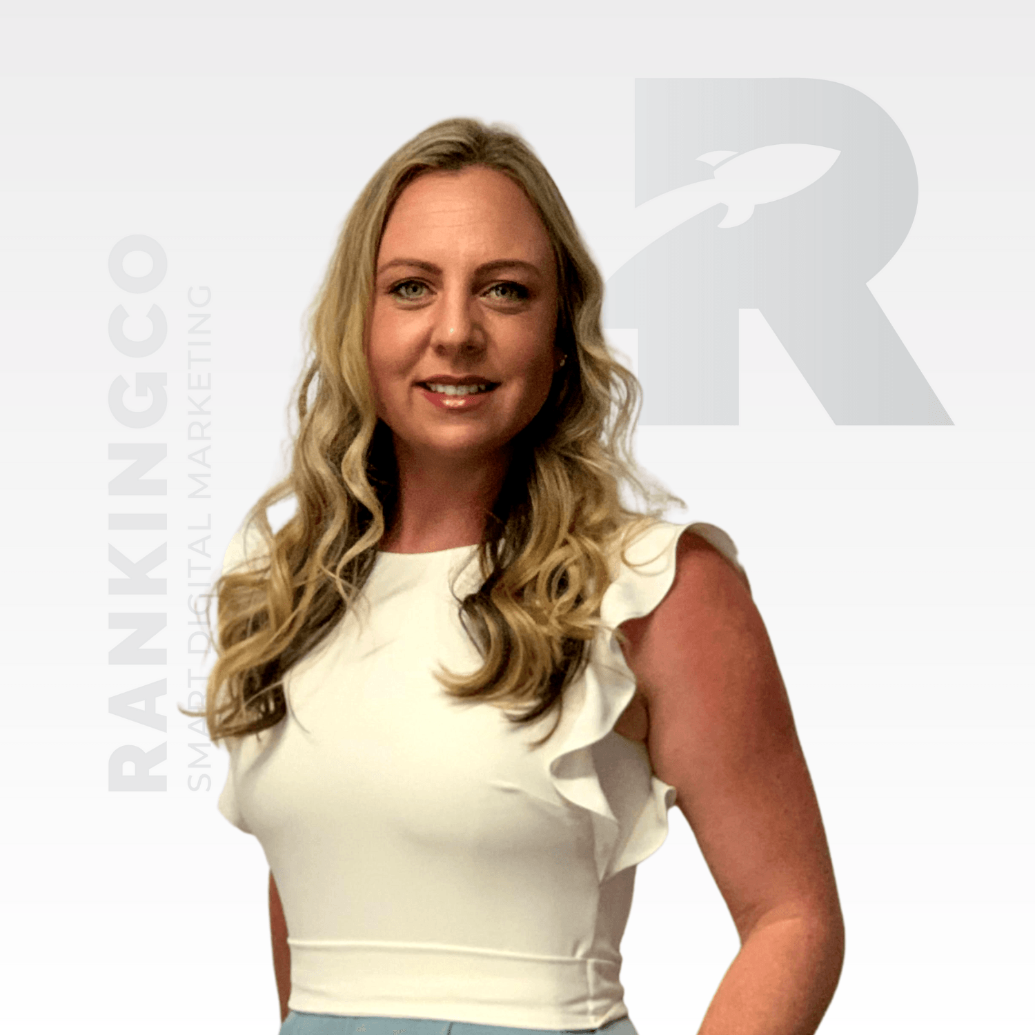A woman in a white top stands in front of a white background with the letter r on it