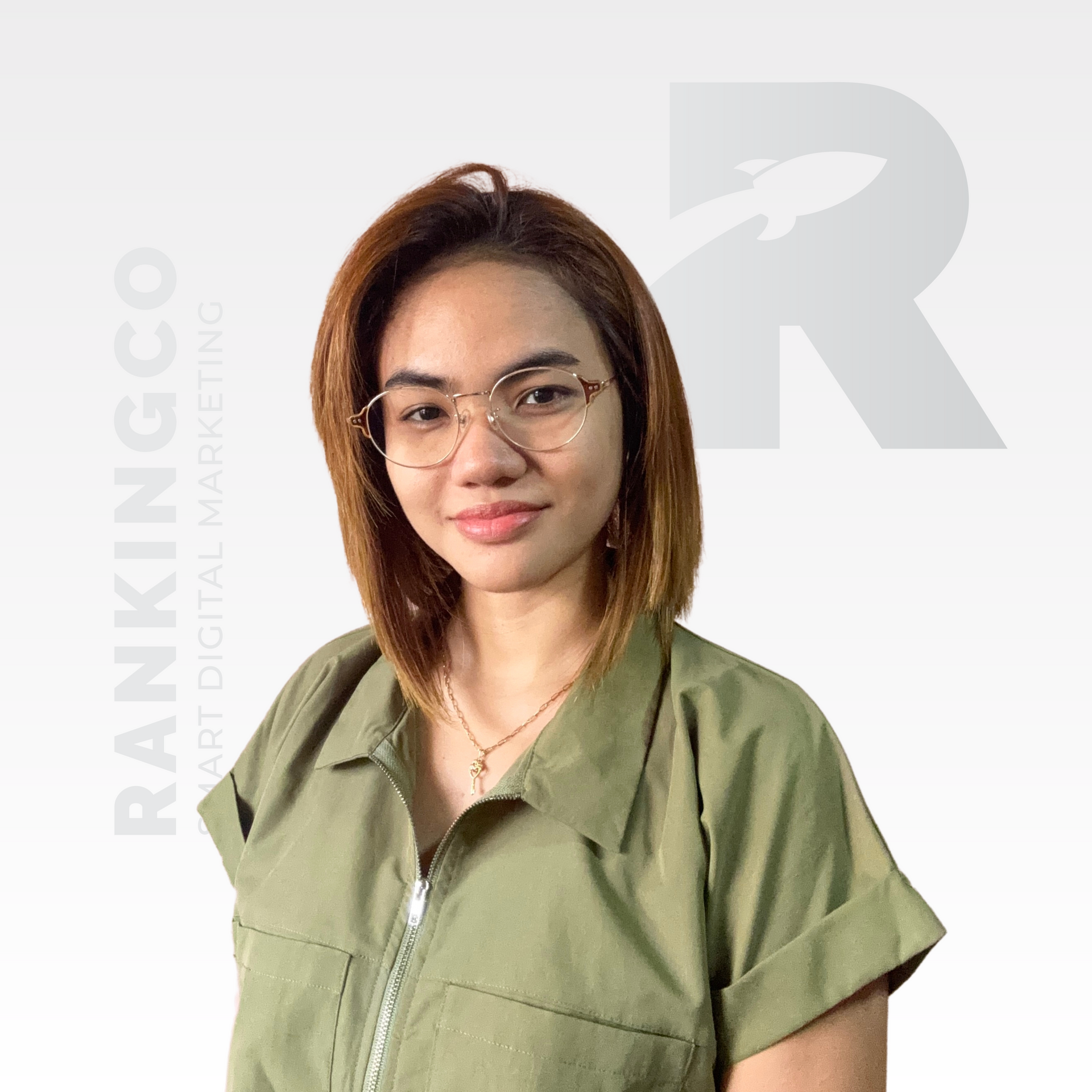 A woman wearing glasses and a green shirt is standing in front of a white background.