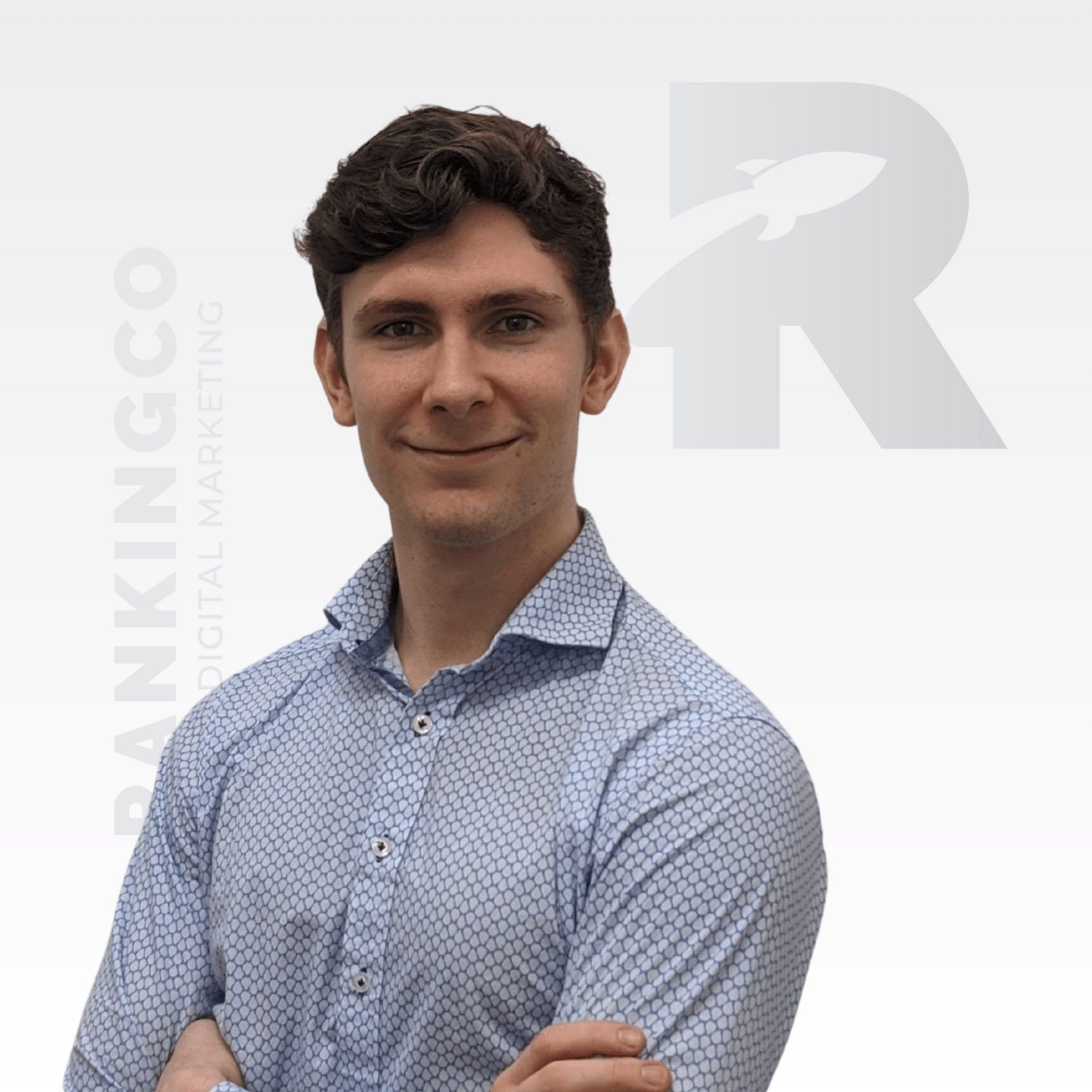 A man stands with his arms crossed in front of a sign that says ranking co