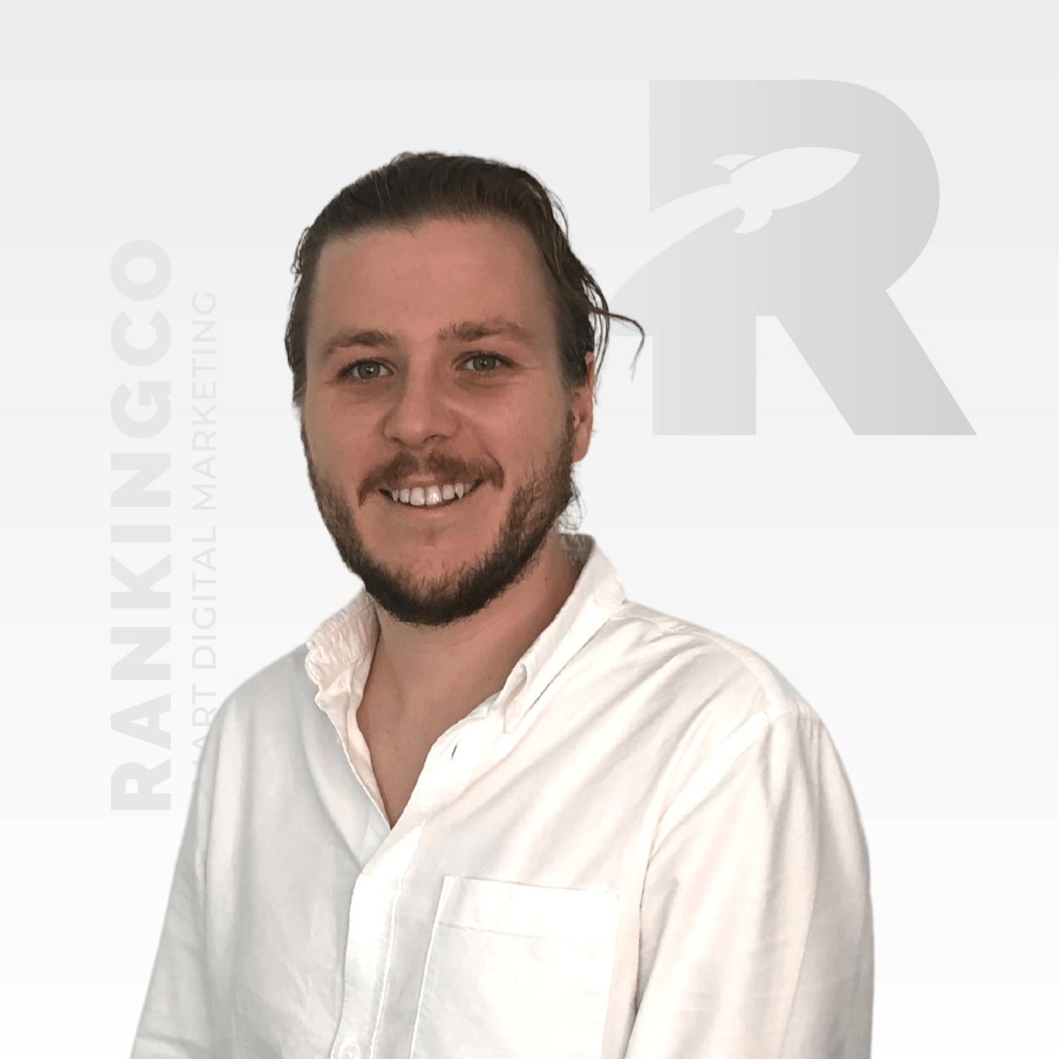 A man with a beard wearing a white shirt is smiling