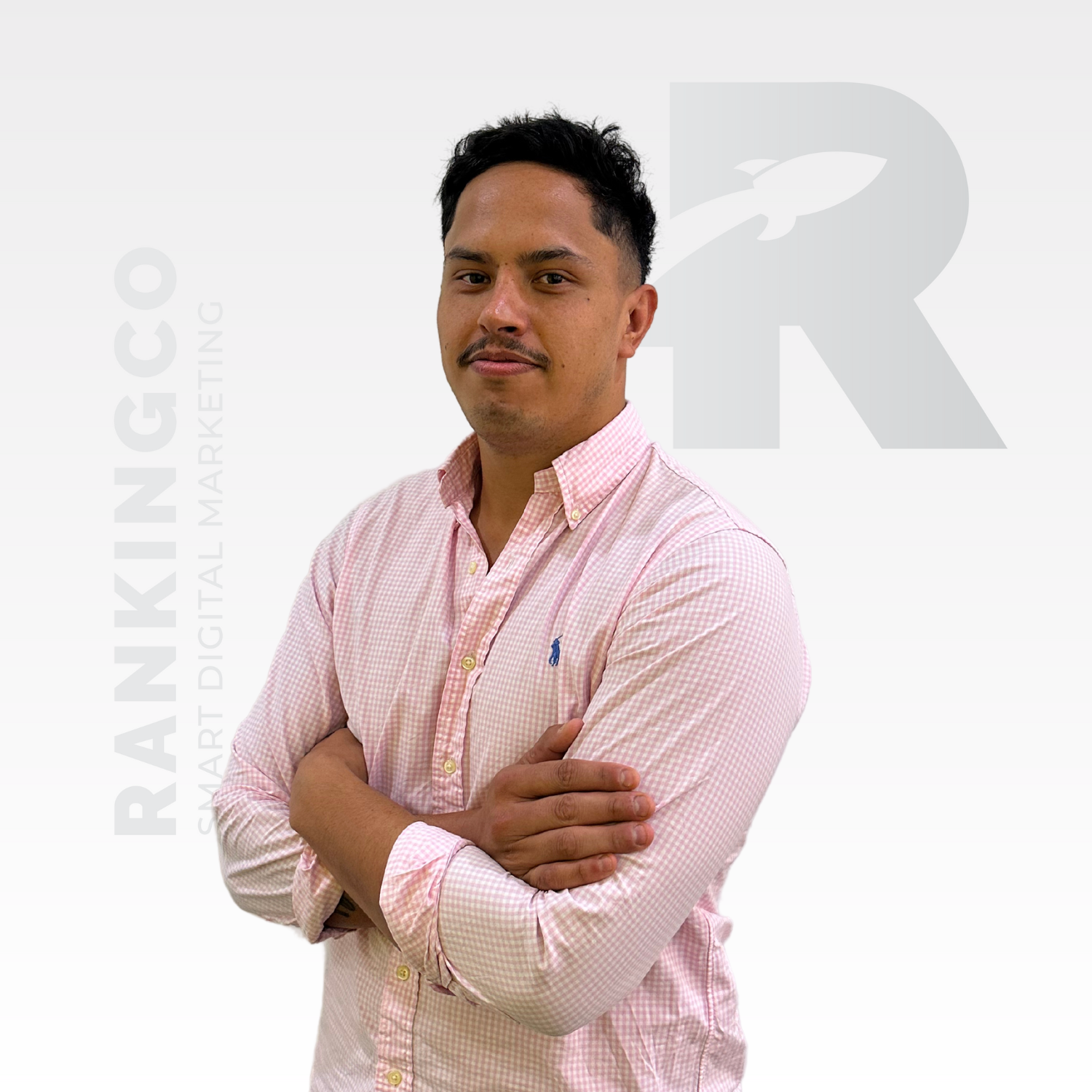 A man in a pink shirt is standing with his arms crossed.