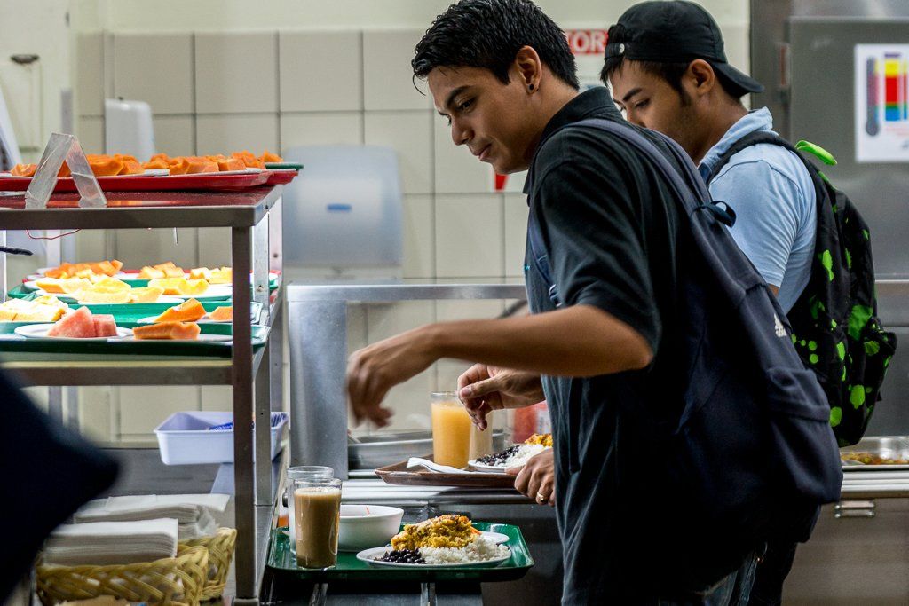 A group of young men are standing in a kitchen eating food from a tray.