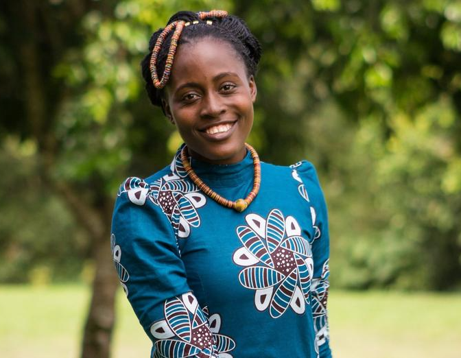 A woman wearing a blue dress and a necklace is smiling for the camera.
