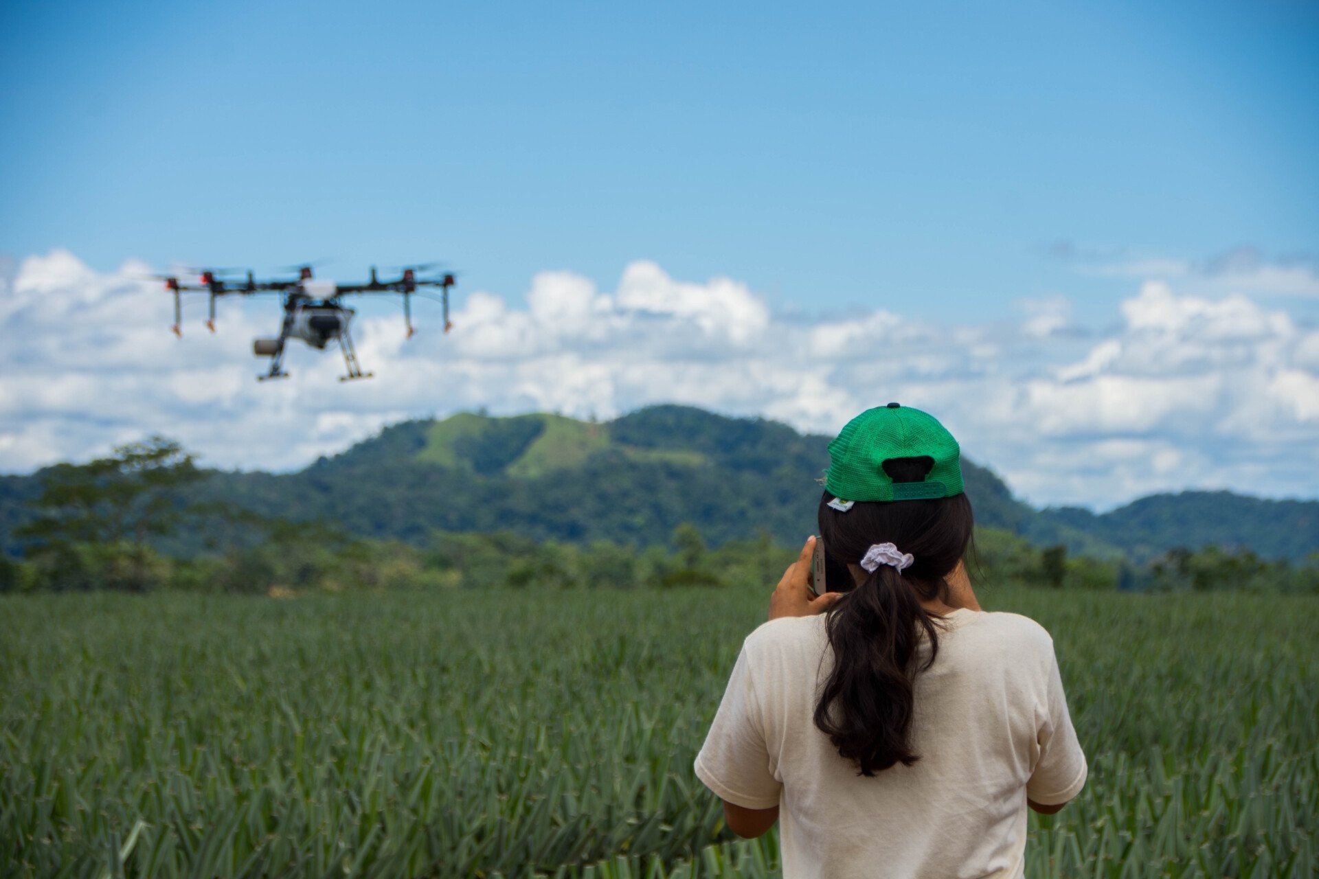 A woman is looking at a drone flying over a field.