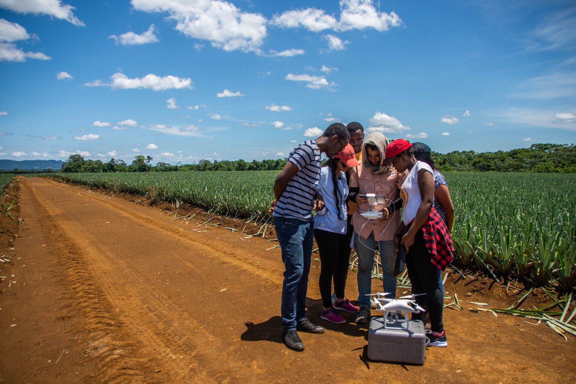 A group of people are standing on a dirt road looking at a drone.