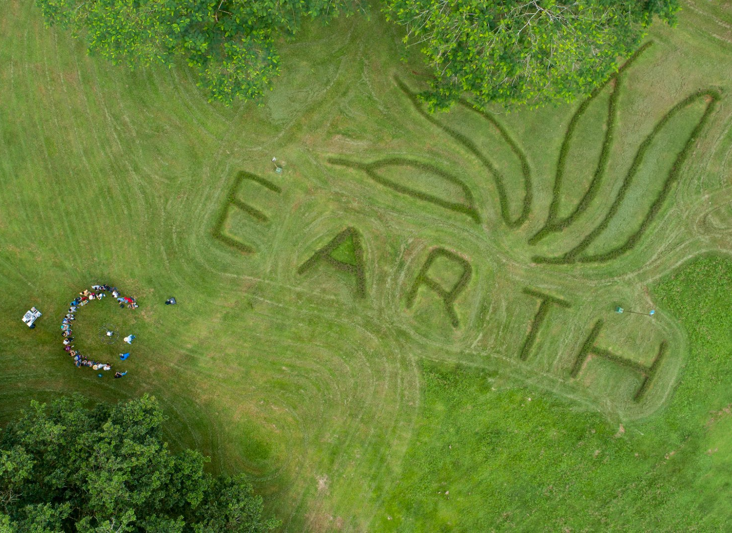 An aerial view of a group of people standing around the word EARTH written in the grass.