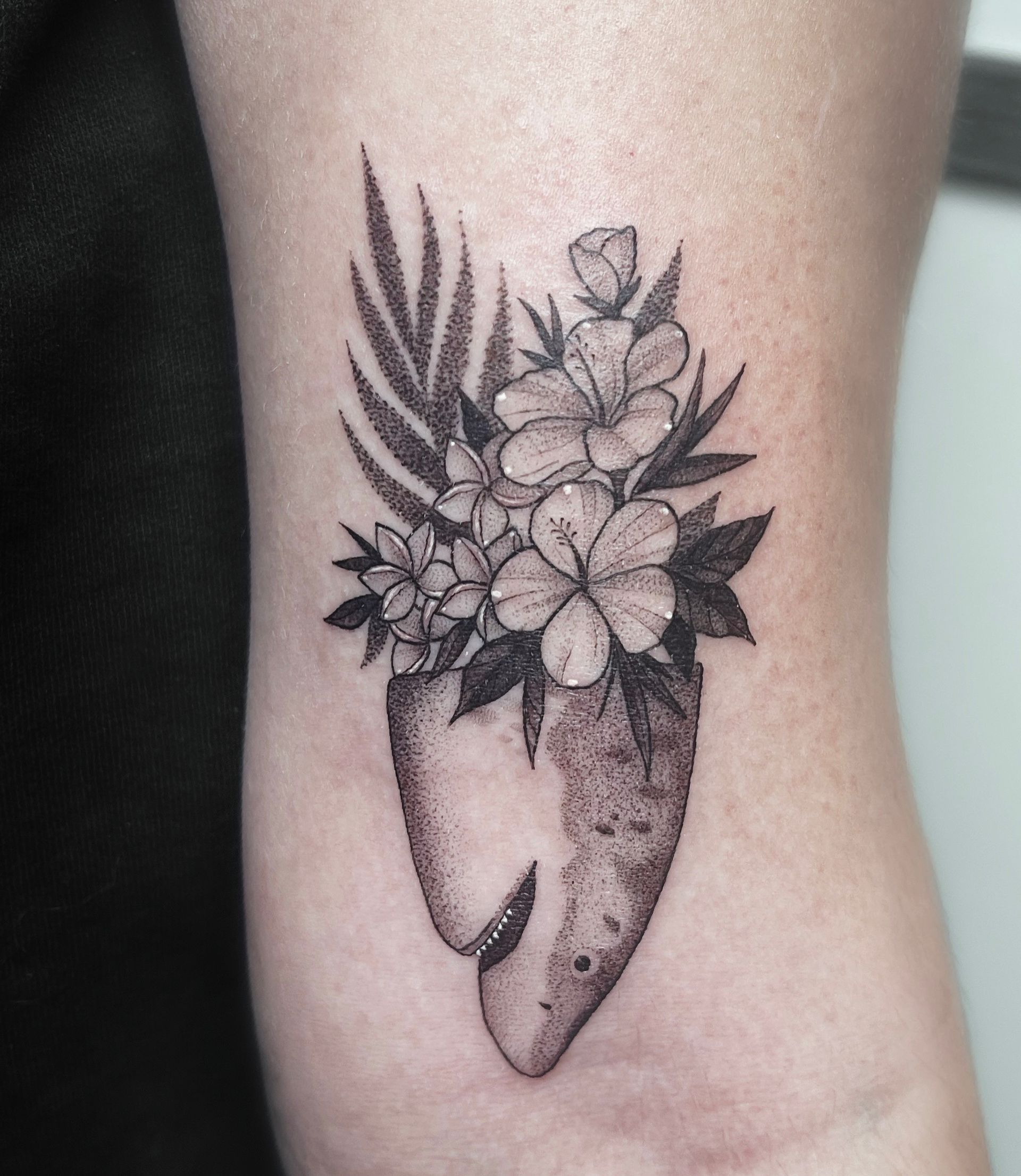 Black and white floral tattoo on arm, featuring stylized flowers and foliage in a shark's head.