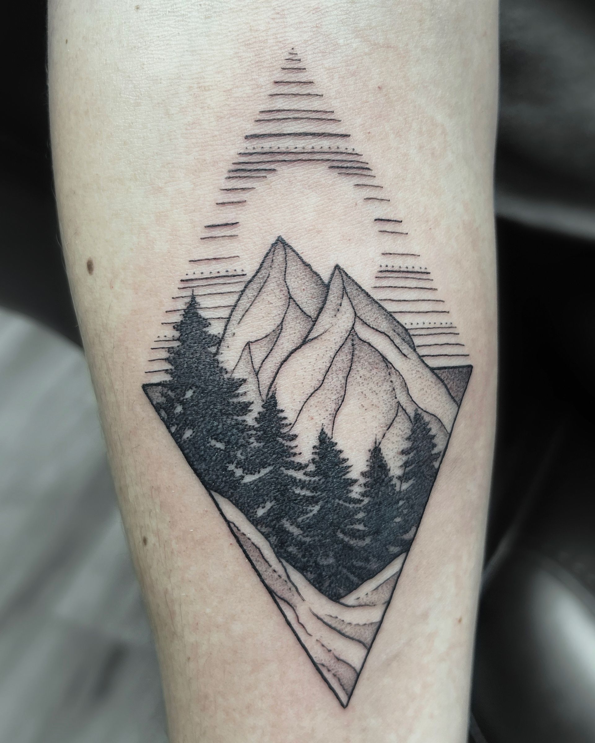 Tattoo on arm: Diamond shape with mountain range, pine trees, and horizontal lines.
