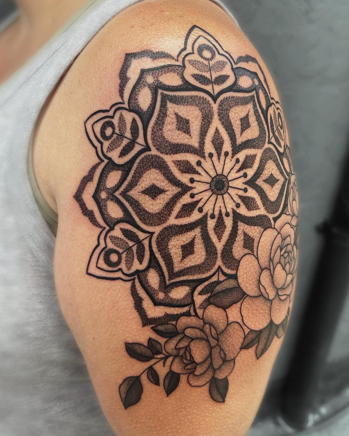 Tattoo on a shoulder of a black mandala with flowers and leaves.