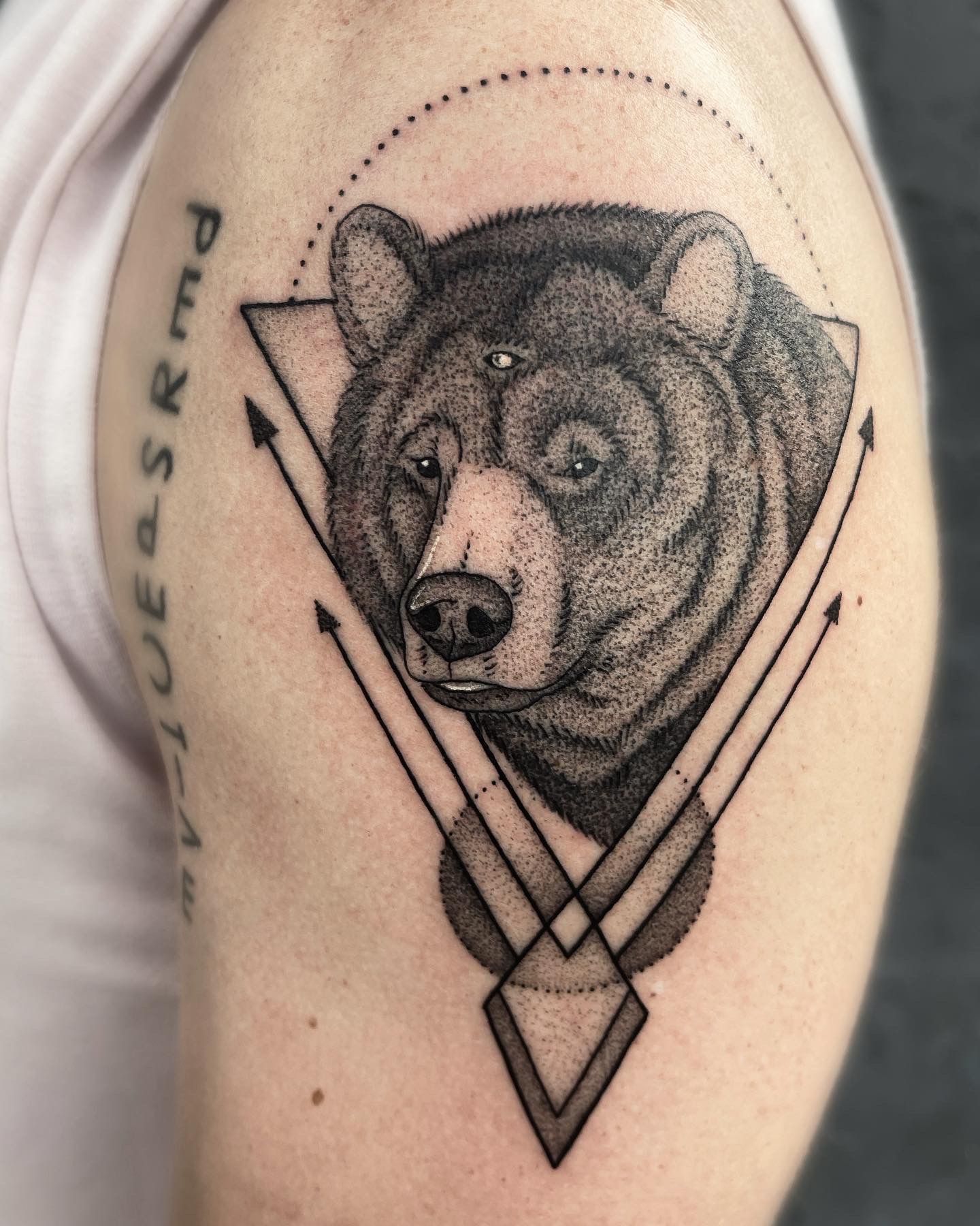 Bear tattoo on an arm, with geometric shapes, dot shading, and arrows.