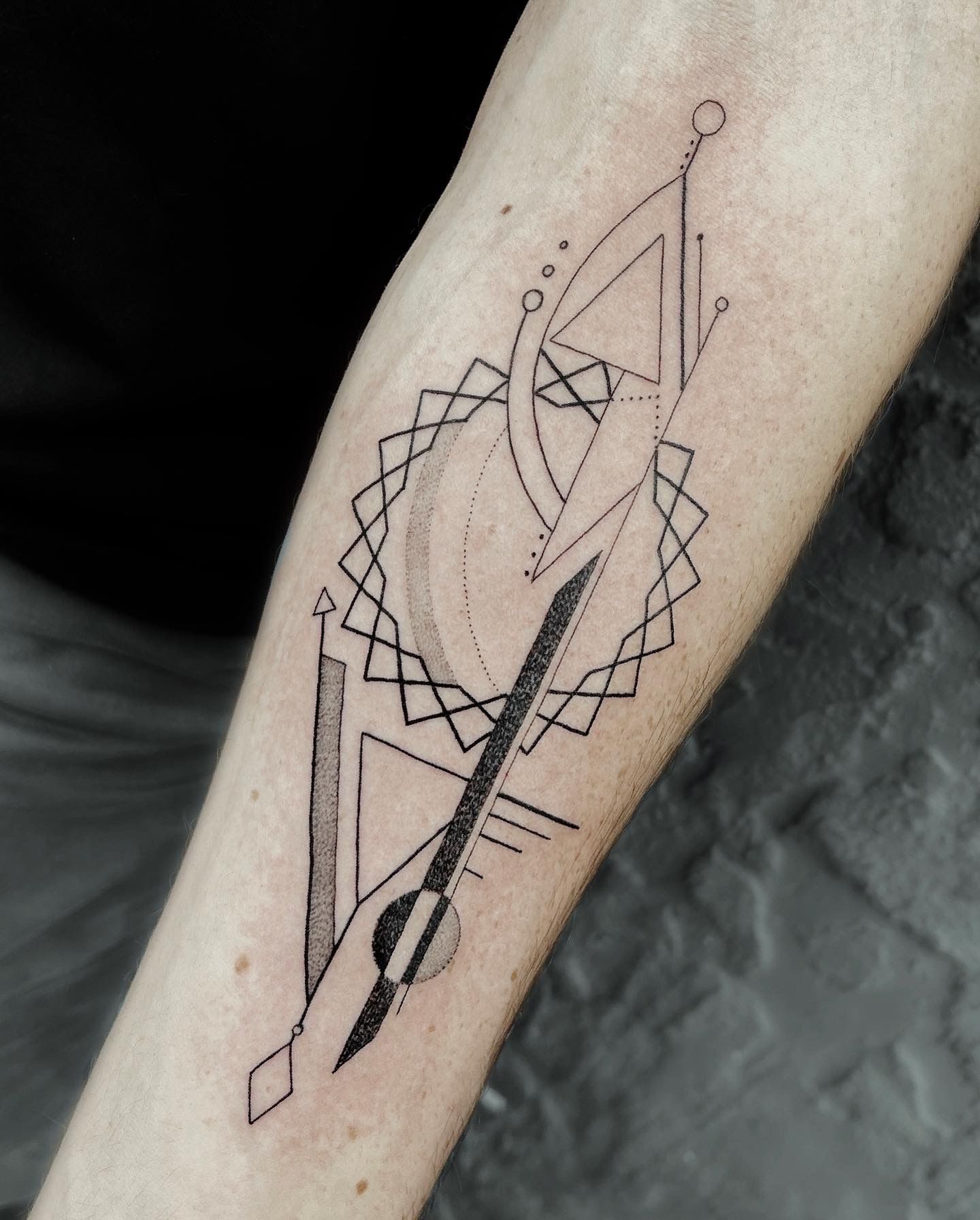Geometric tattoo on forearm: black lines and shapes, arrow, geometric patterns, and crescent.