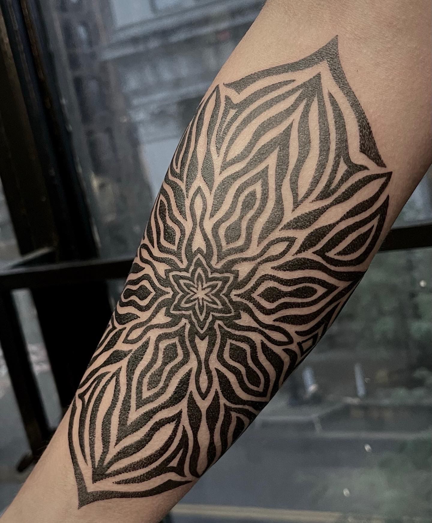 Black mandala tattoo on forearm, intricate zebra-like pattern design.