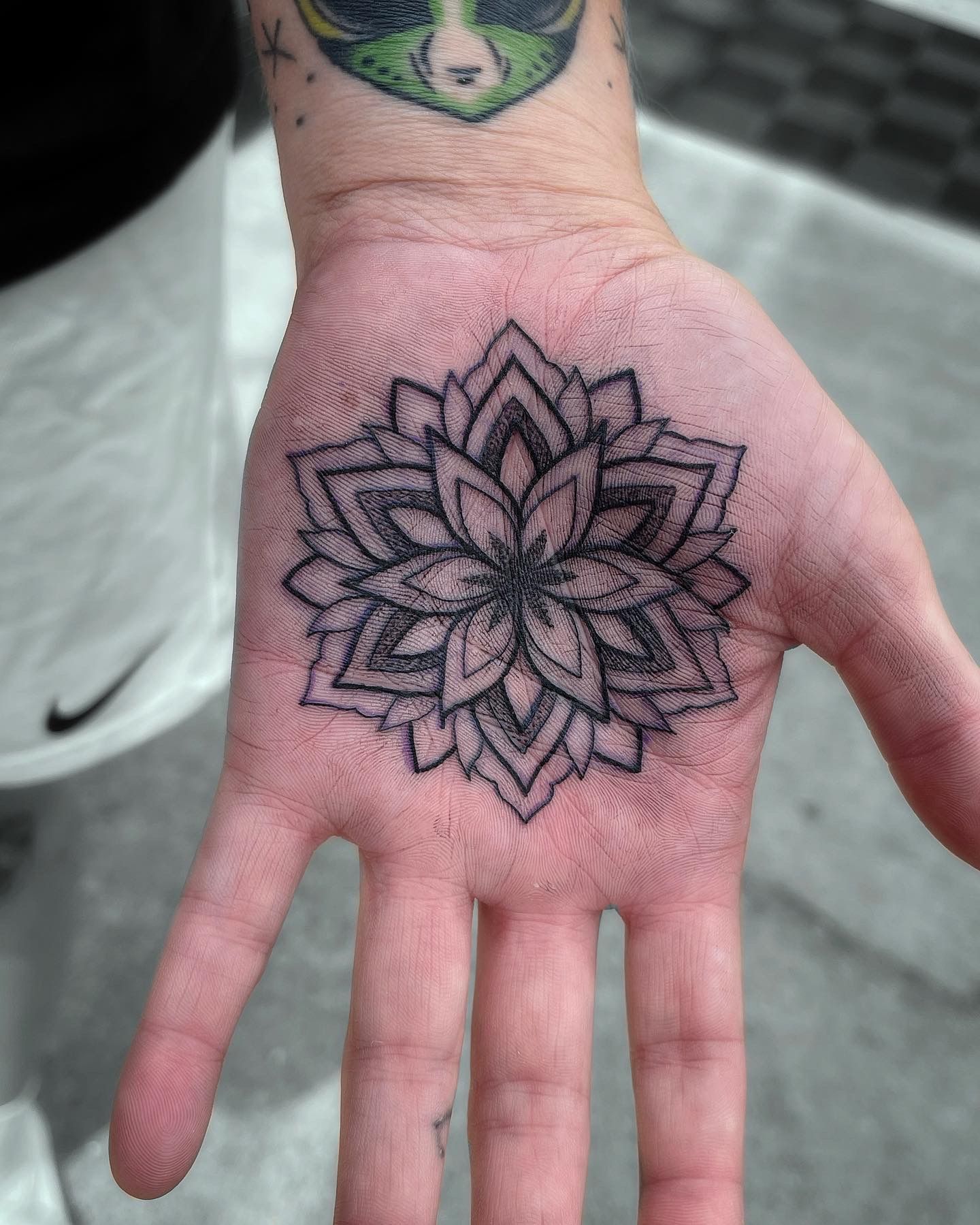 Hand with mandala tattoo on palm, alien tattoo on wrist.