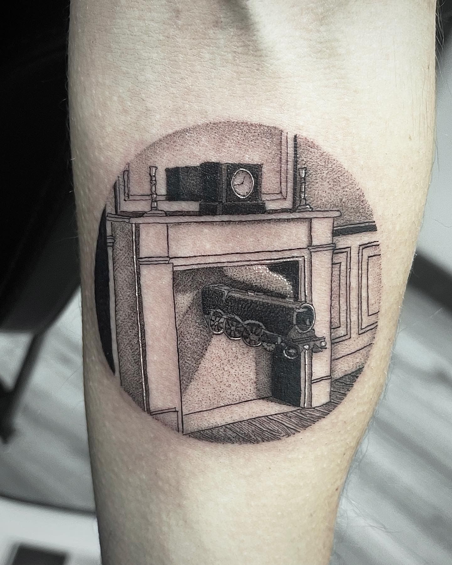 Tattoo of a fireplace inside a circle on a forearm. Black and white, detailed shading.
