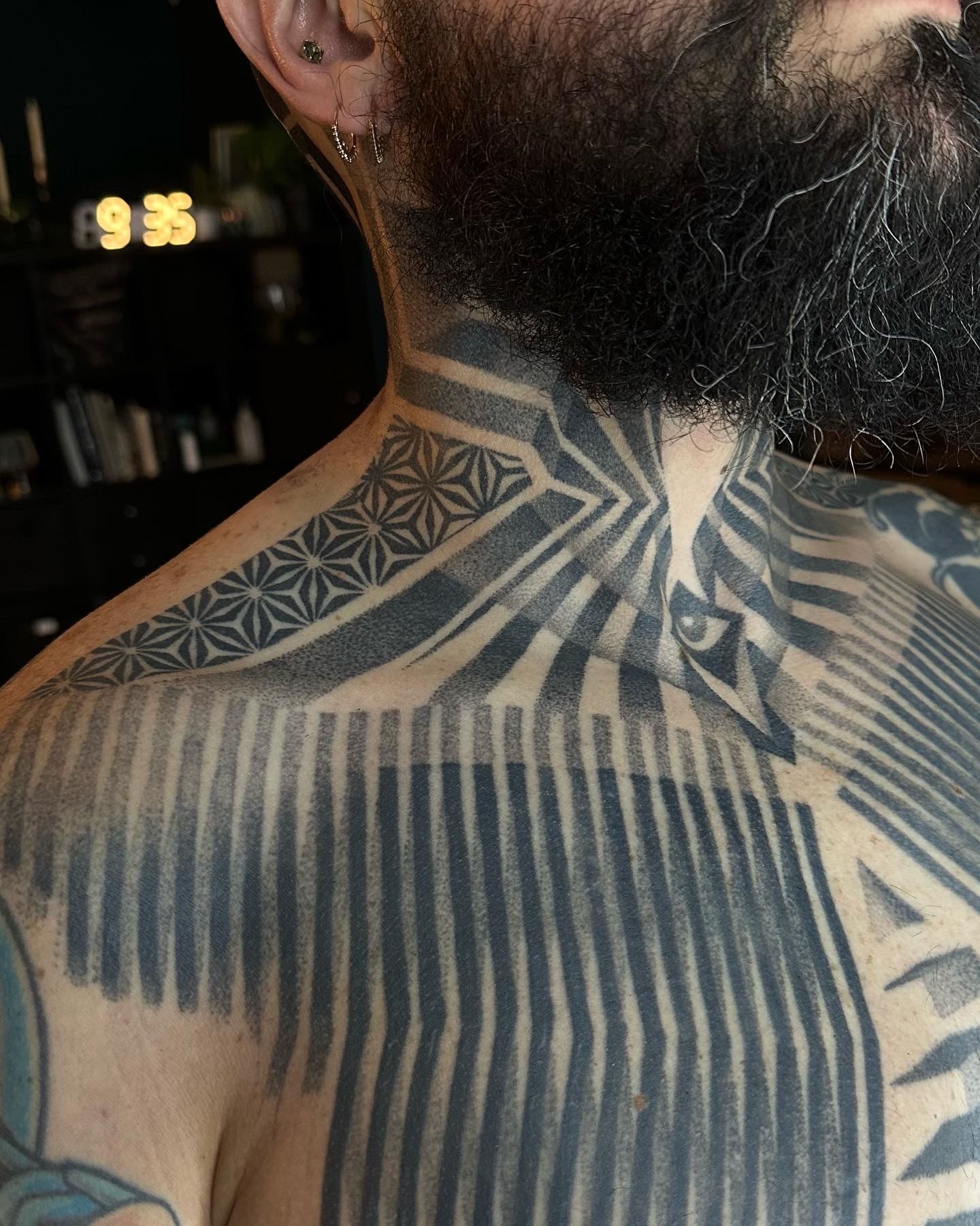 Man with a detailed black neck and chest tattoo featuring geometric and striped patterns.