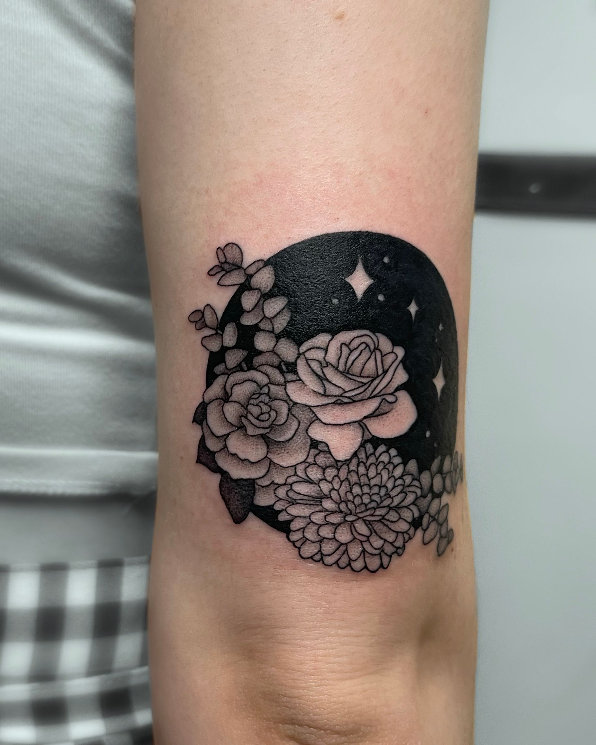 Black and white floral tattoo on an arm, with a dark background and stars.