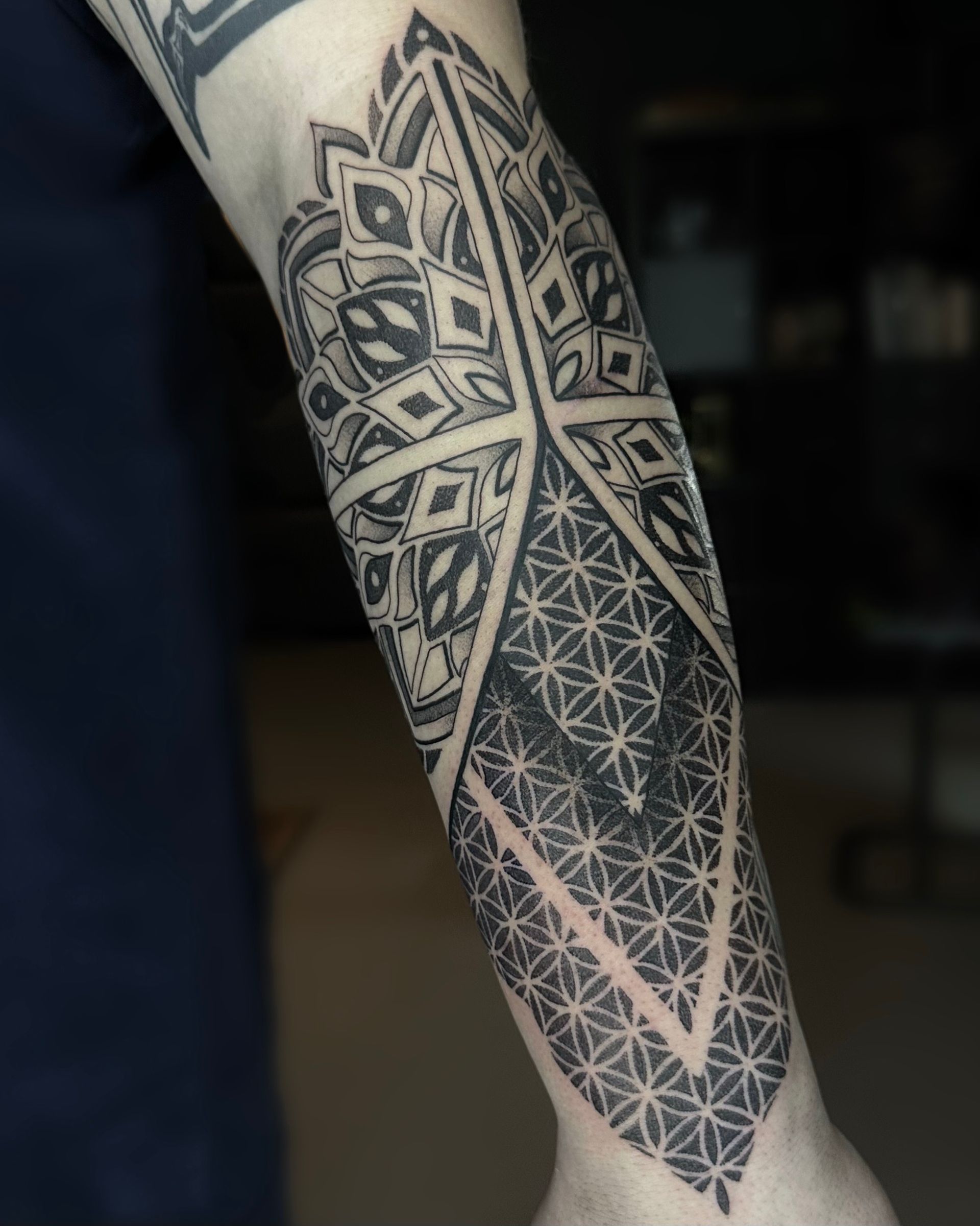 Black geometric tattoo on an arm, featuring mandala and mosaic patterns.