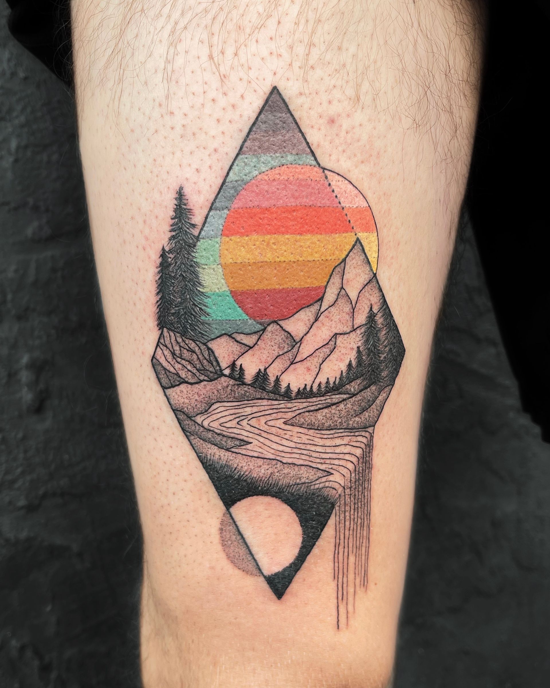 Tattoo of a mountain landscape with a colorful sunset, contained within a diamond shape.