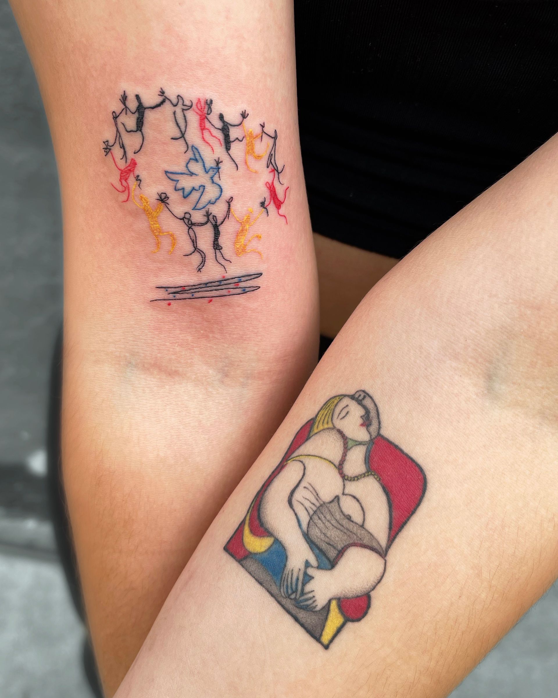 Two arm tattoos: abstract figures dancing and a Picasso-esque embrace in red, yellow, and blue.