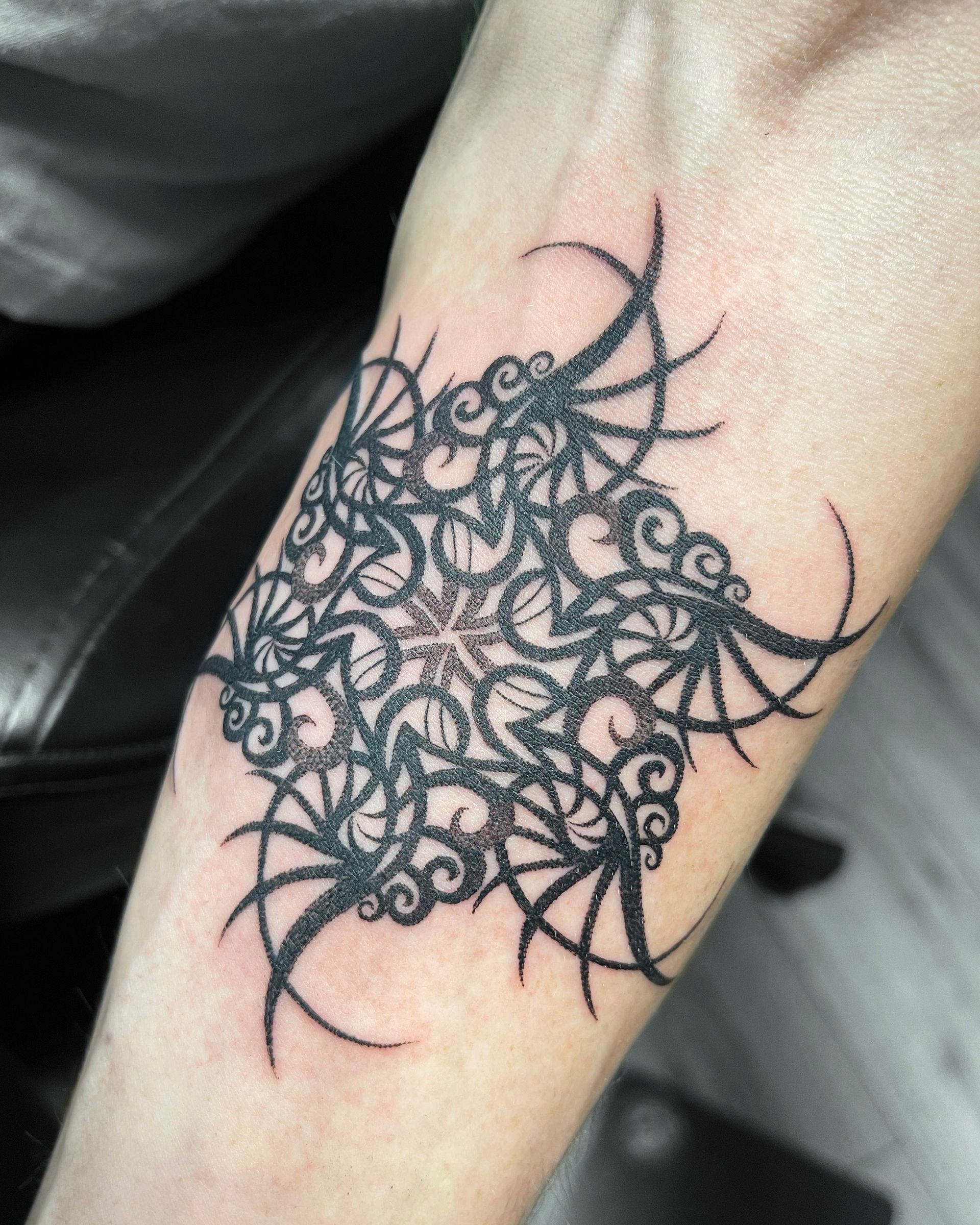 Black dotwork tattoo on a forearm, a complex geometric design radiating from a central point.