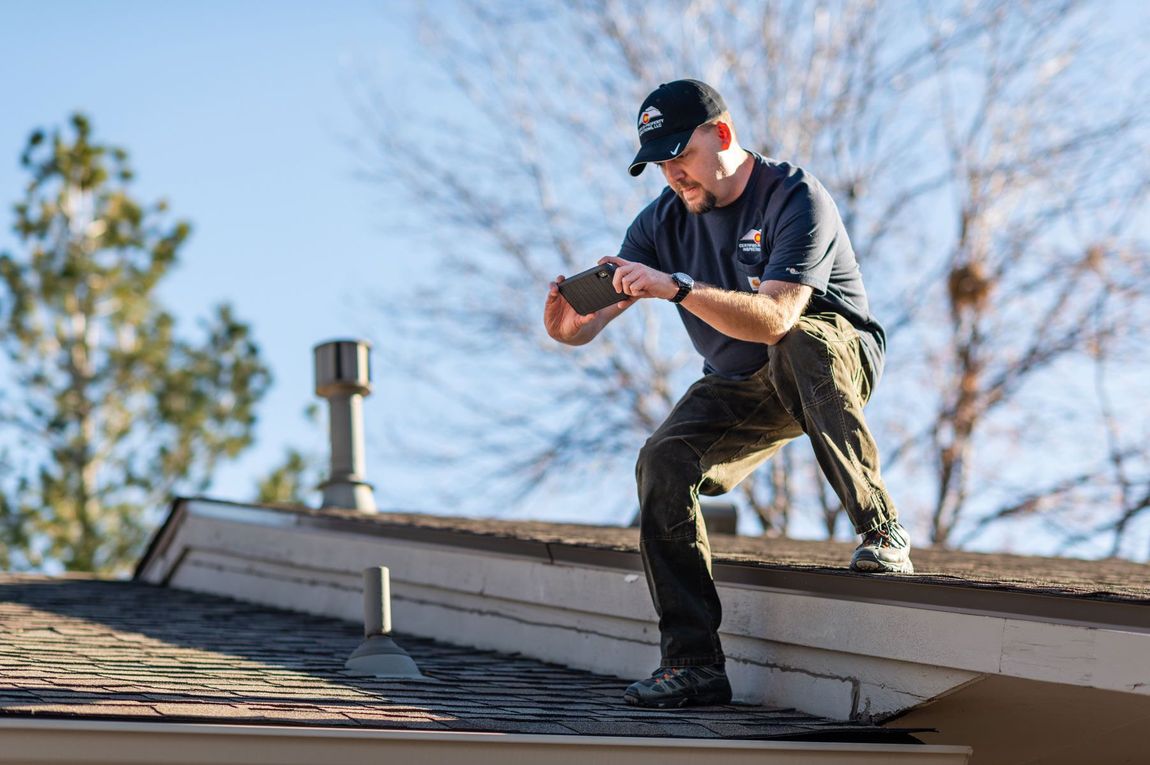 A man is kneeling on the roof of a house looking at something.