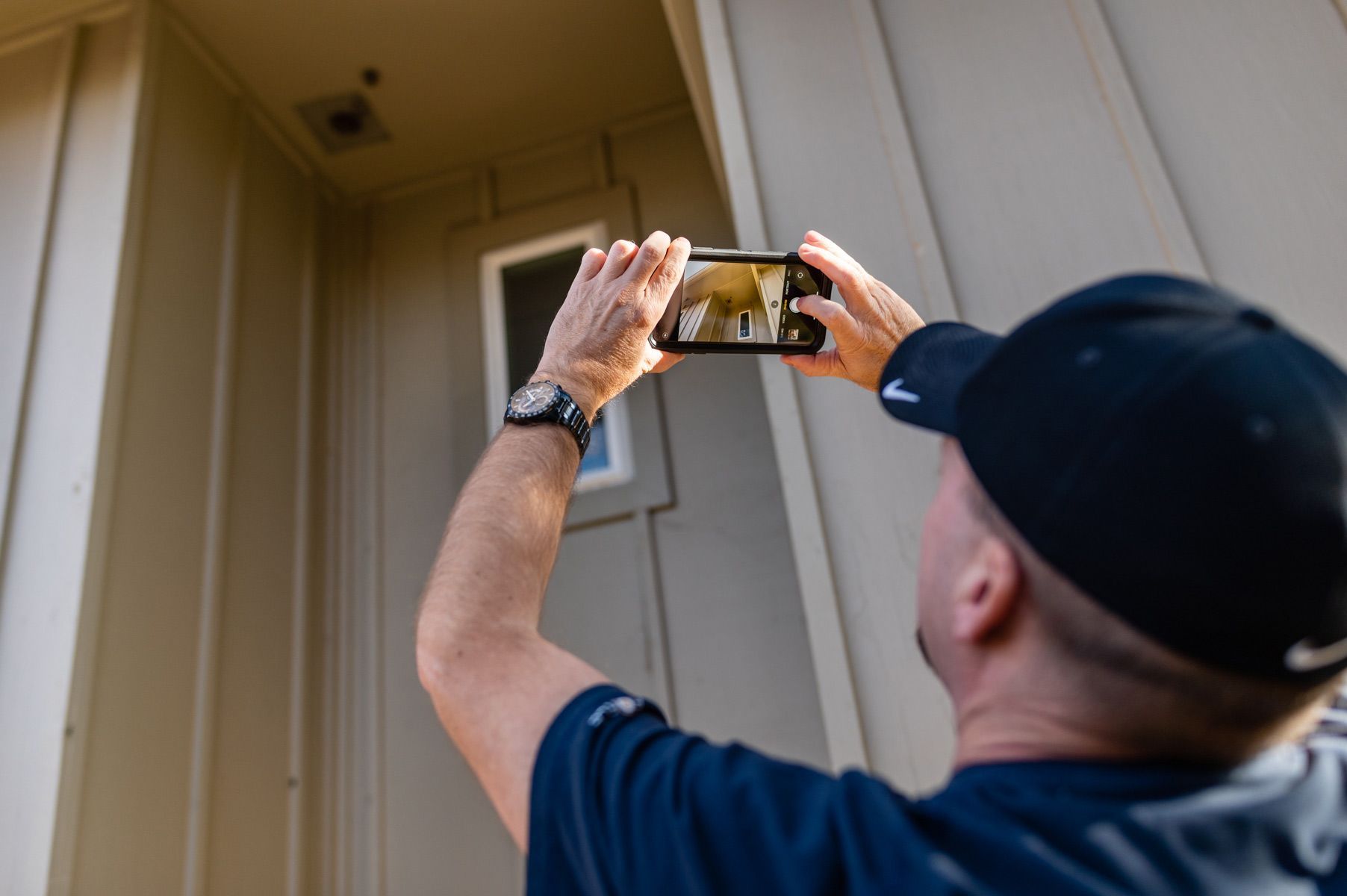 A man is taking a picture of a house with a cell phone.