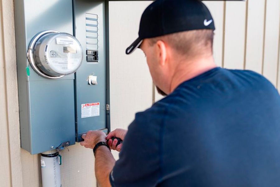 A man in a black hat is working on an electrical box.