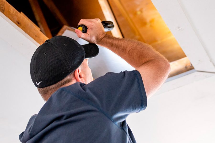 A man is using a screwdriver to fix a hole in the ceiling.