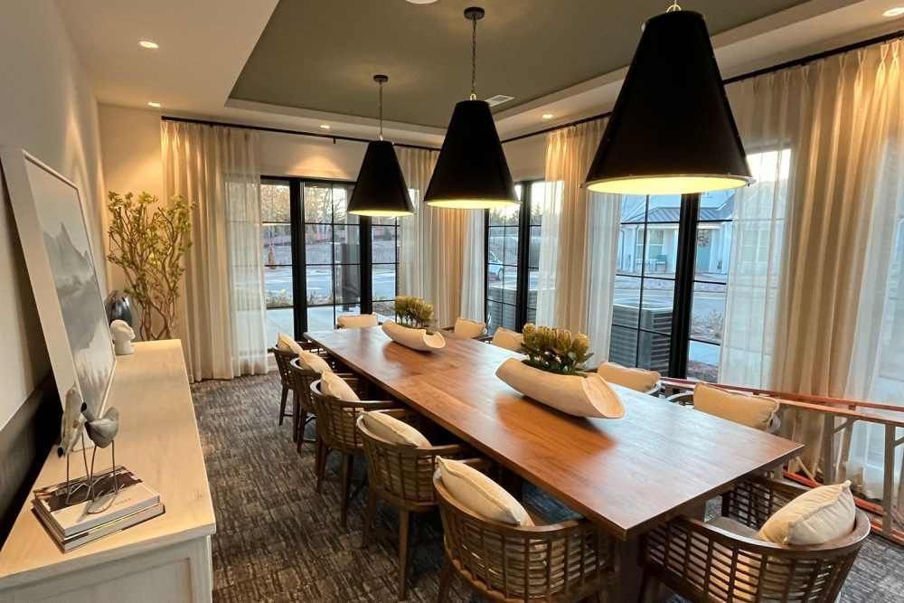 A long wooden dining table with chairs, topped with white vases, under three black pendant lights in a modern room.