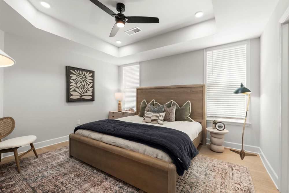 Bedroom with gray walls, wood bed frame, rug, and ceiling fan at Hayloft Big Creek, offer 55+ homes for rent in Alpharetta, GA.