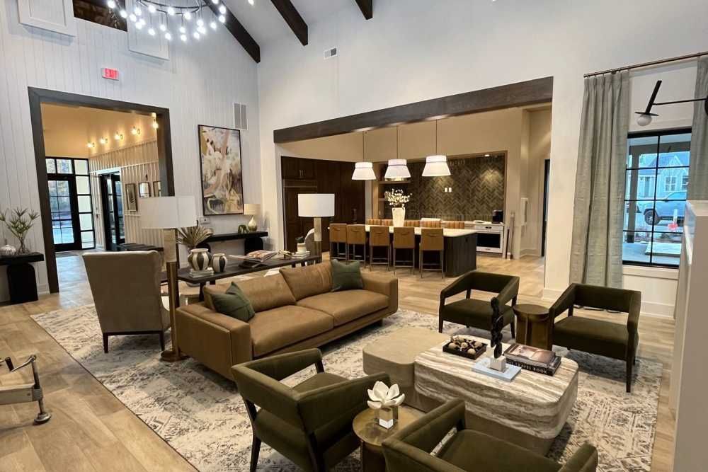 Spacious open-concept living area with couches, chairs, and a kitchen island. Natural light, neutral colors.